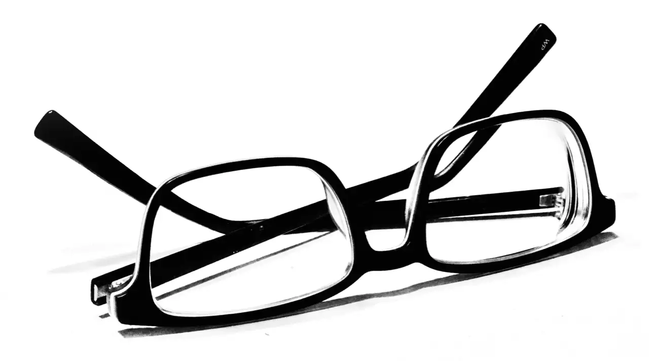 Black plastic-rimmed eye glasses, isolated, folded up lying on a white surface.
